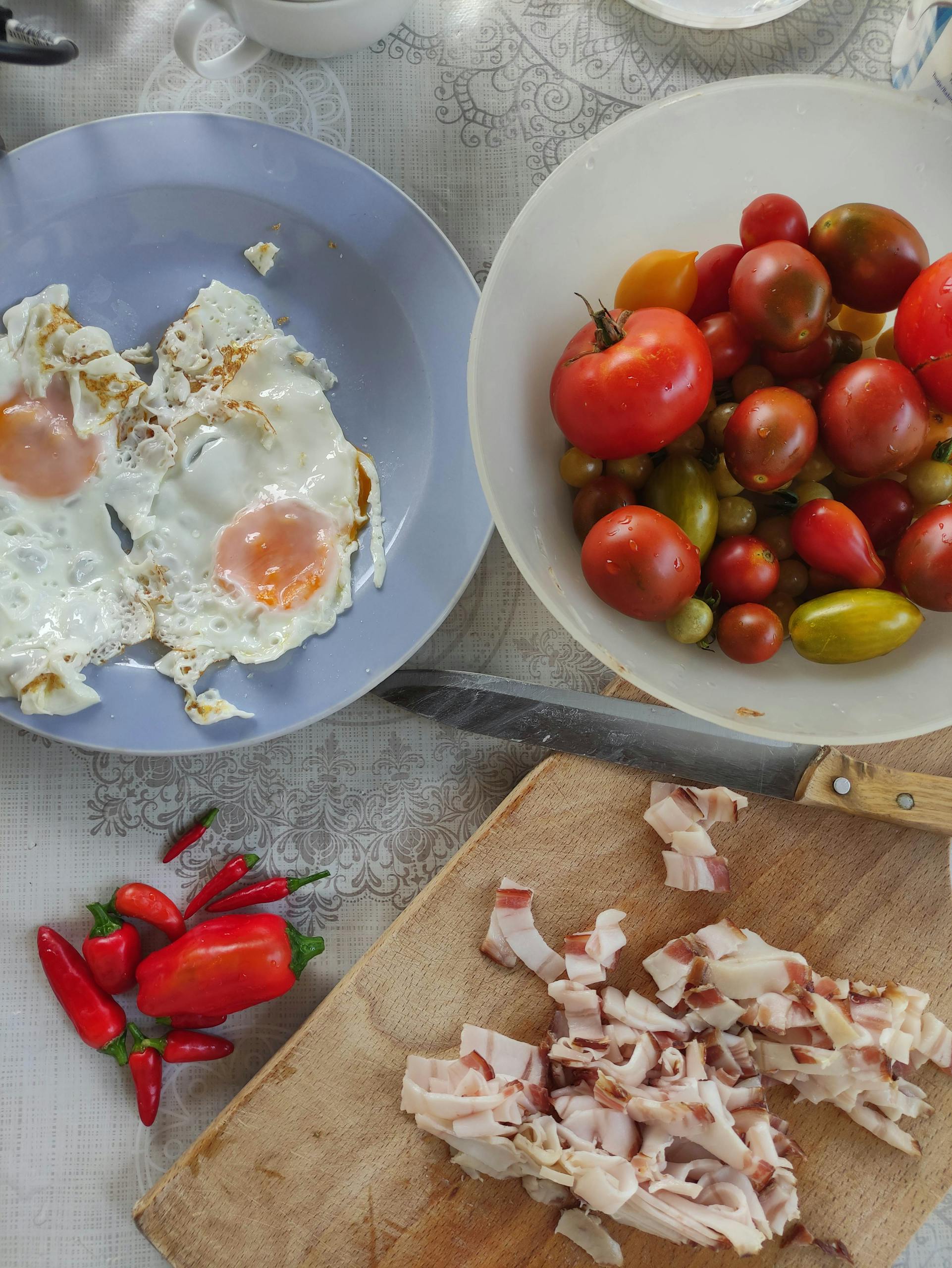Bright overhead view of a breakfast spread featuring fried eggs, assorted tomatoes, and chopped bacon.
