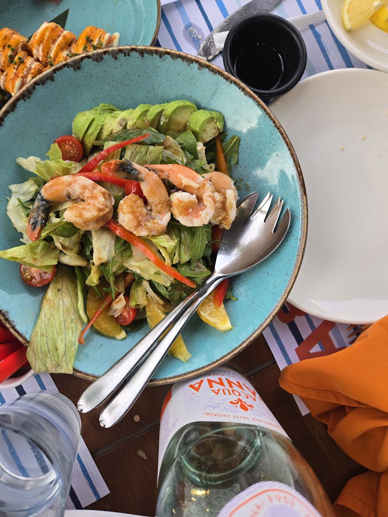 Vibrant shrimp salad with fresh vegetables in a blue bowl on a wooden table.